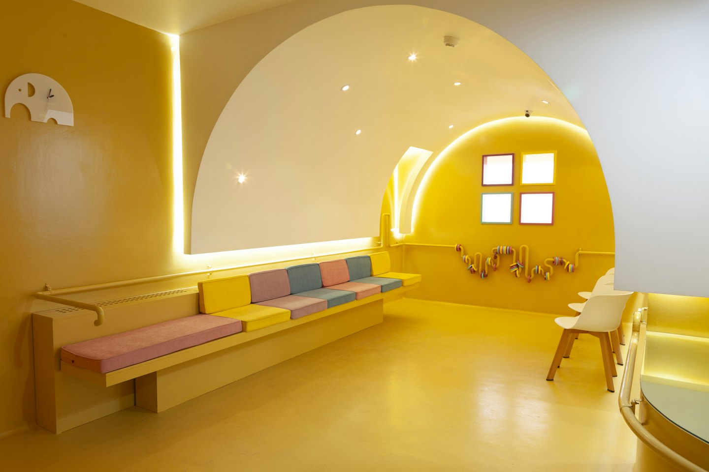 Página Inicial Modern yellow waiting room with curved architecture and interactive wall panel.